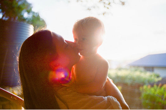 mother kissing baby on cheek with sunset shining in the background