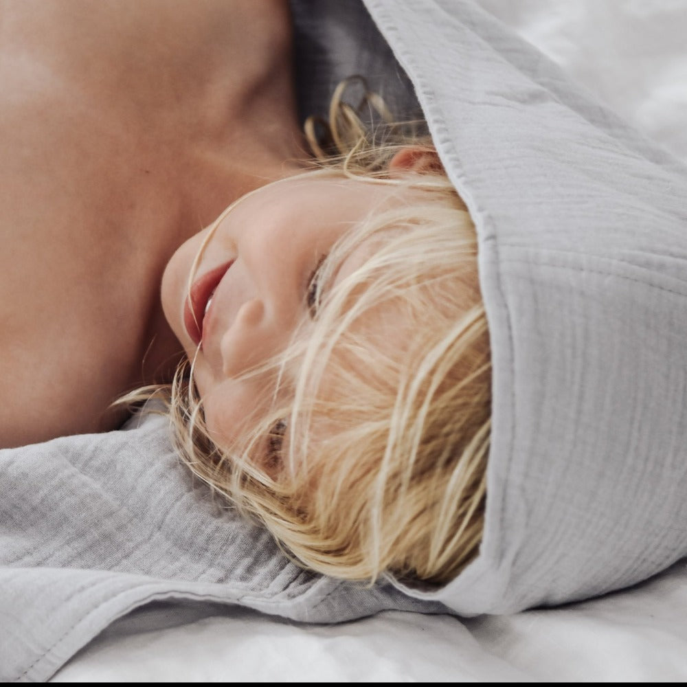 child laying down on side wearing the light mist blue organic hooded cotton towel on her head