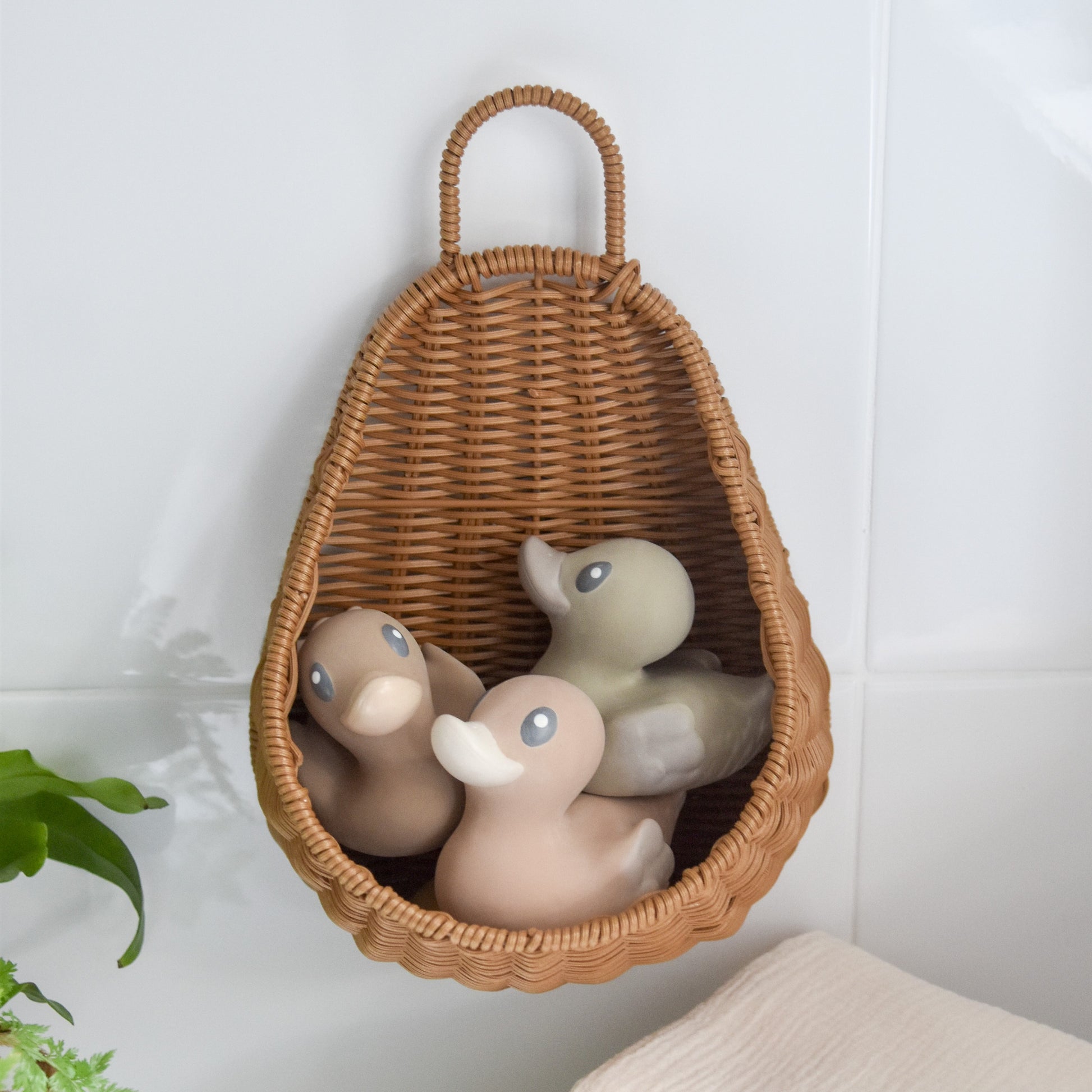 bath storage basket woven from recycled plastic rattan, attached to a bathroom wall with a suction cap, storing three rubber duck bath toy