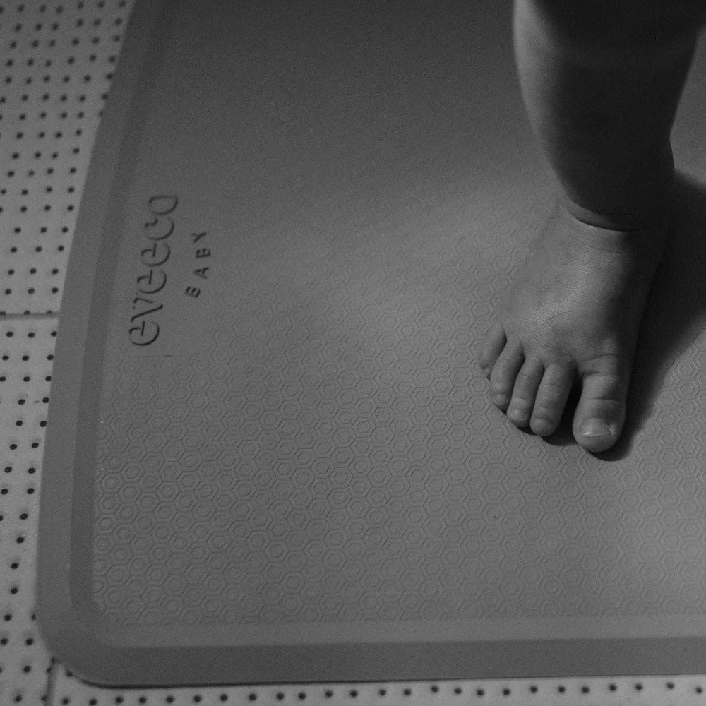 close view of a toddlers foot standing on a large grey natural rubber non-slip bath mat