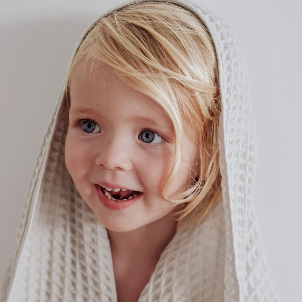 girl smiling while wearing light grey dove coloured organic cotton waffle towel over her head