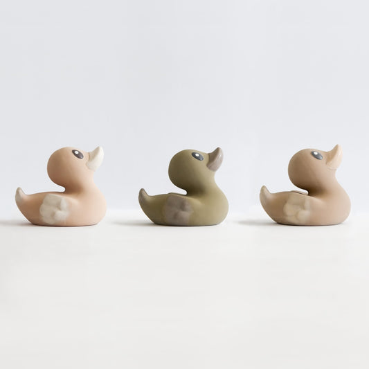 set of three natural rubber bath toys ducks in a line. They are in varying neutral colours. 